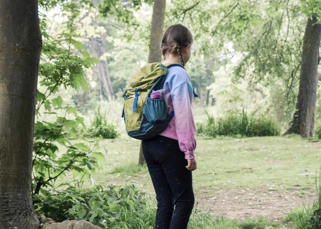 A young girl faces away from the camera wearing a backpack packed for her year 6 residential trip.