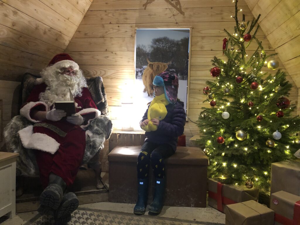 Christmas activities near Cheltenham: Photo of a little girl meeting Santa in a log cabin