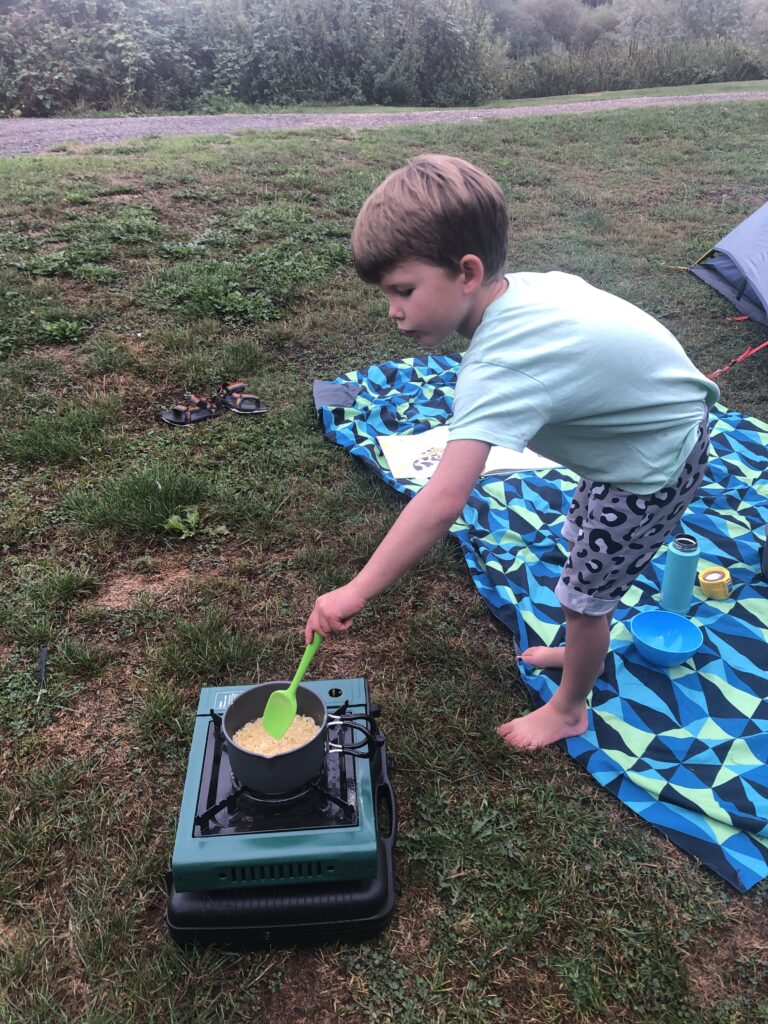 Camping activities: Photo of a 6 year old boy cooking noodles on a camping stove