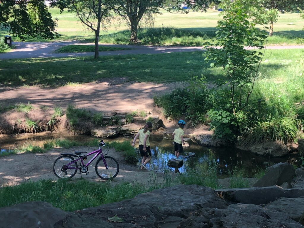 Children crossing a stream using stepping stones, taking part in exercise as a family.