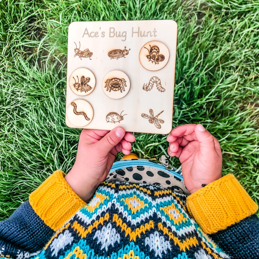 Photo of a young child holding a wooden bug hunt set up by older children.