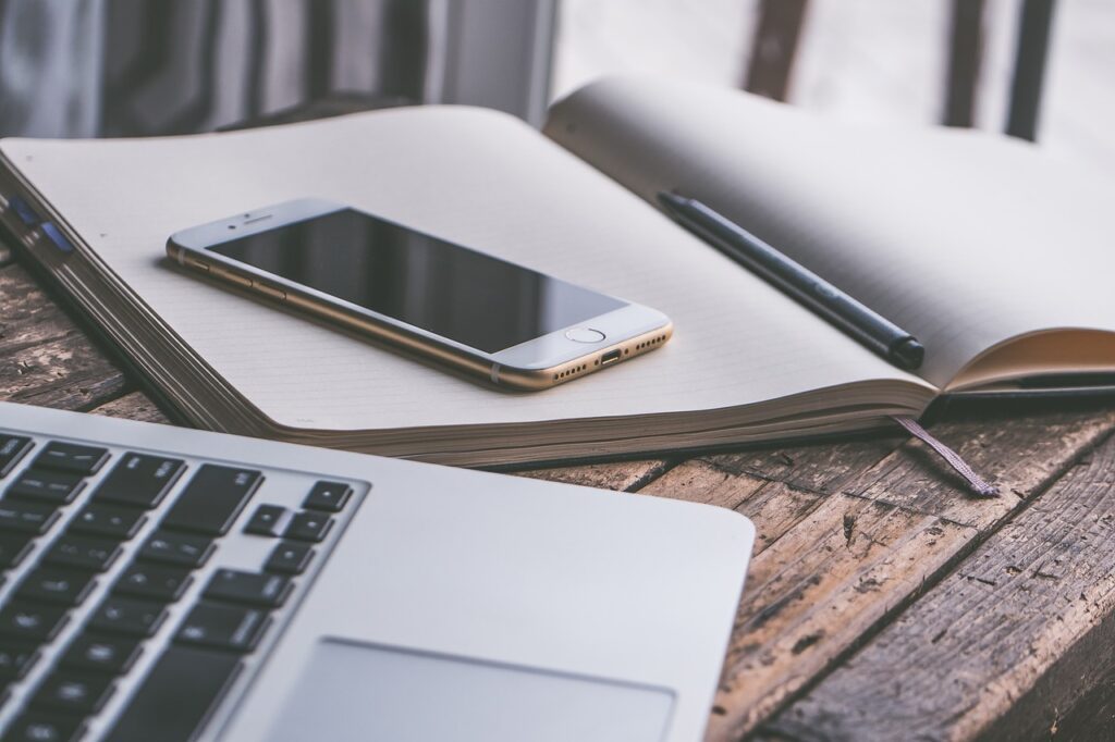 Digital declutter checklist: Photo of an iPhone on top of a paper notepad. These are on a wooden table next to a silver laptop.