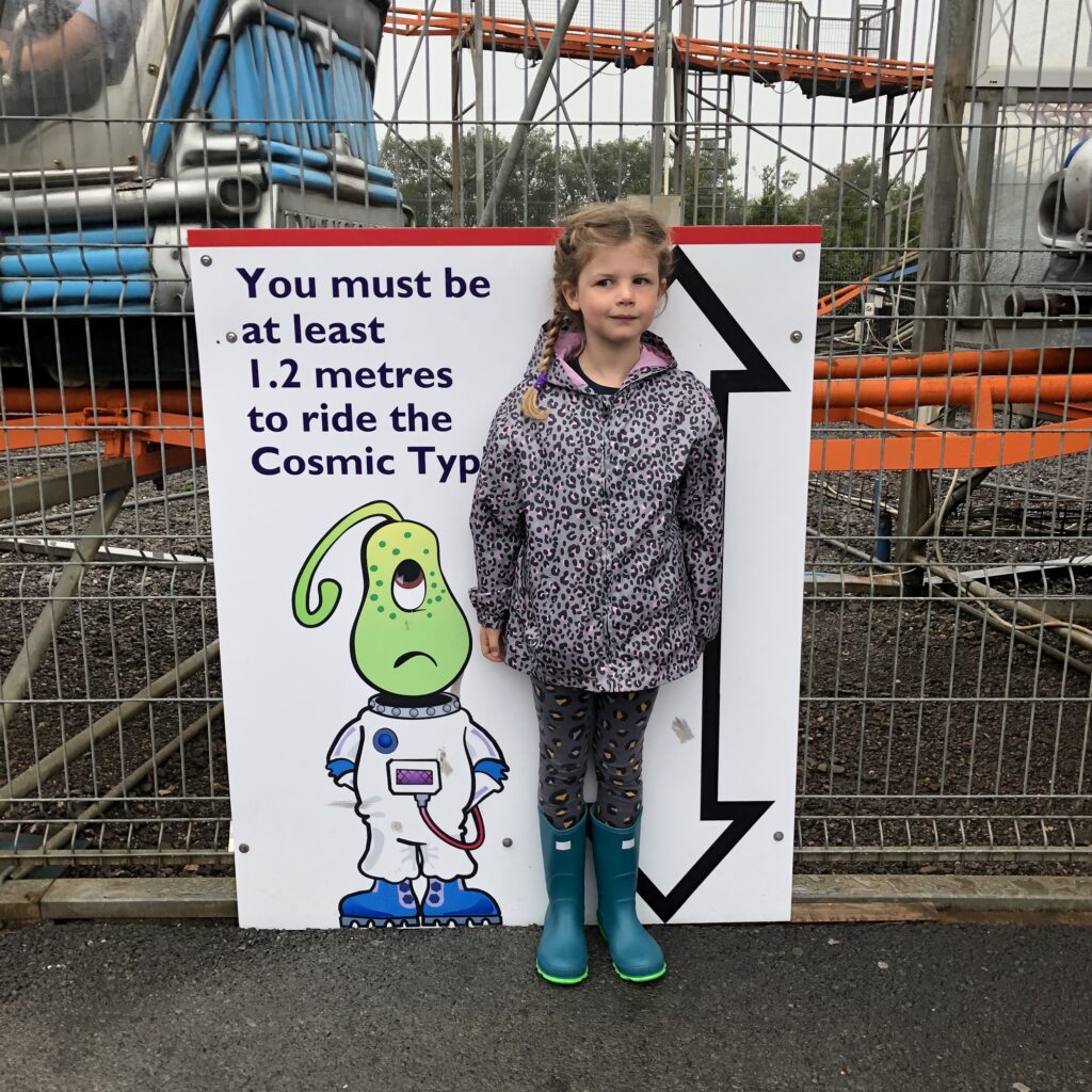 Things to do in North Devon: A photo of a young girl standing next to a height chart near a rollercoaster.