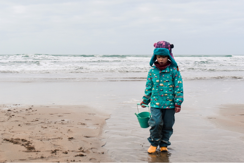 6 year old boy holding a turquoise Scrunch bucket while walking on the beach